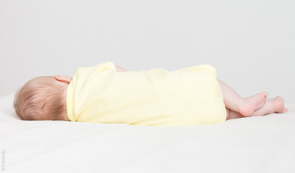 Materac 60x120 cm na którym leży niemowlę w żółtym ubranku.