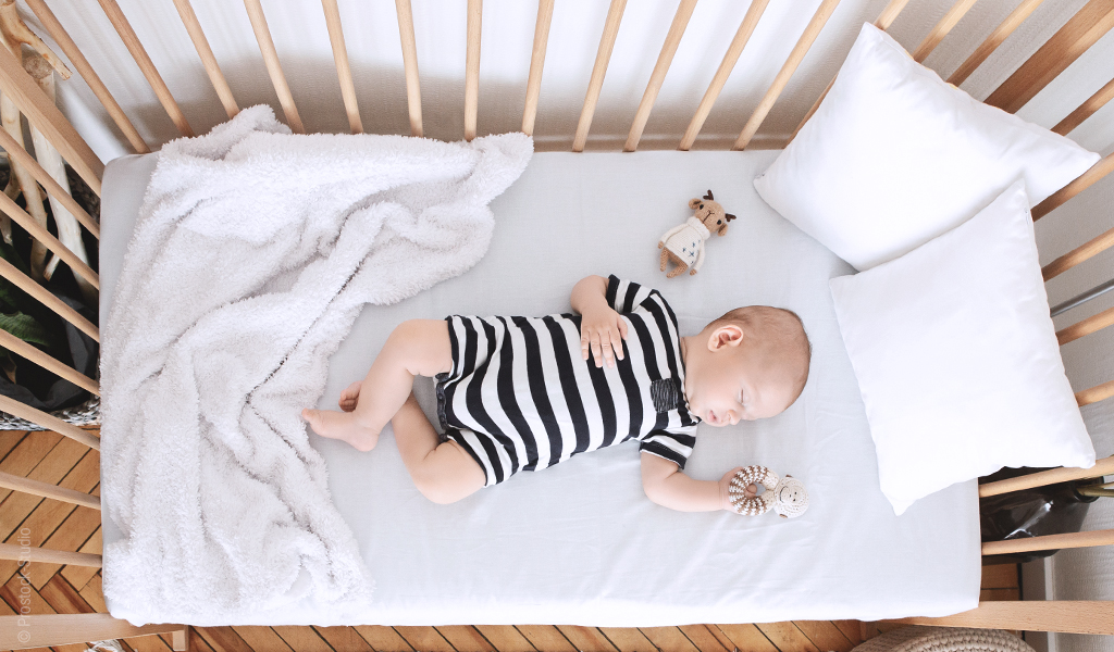Materac dziecięcy 60x120 w łóżeczku, a na nim śpiące niemowlę.