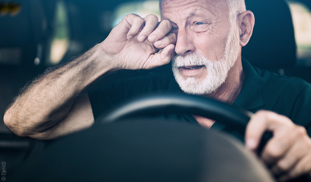 Starszy mężczyzna za kierownicą przecierający oczy
